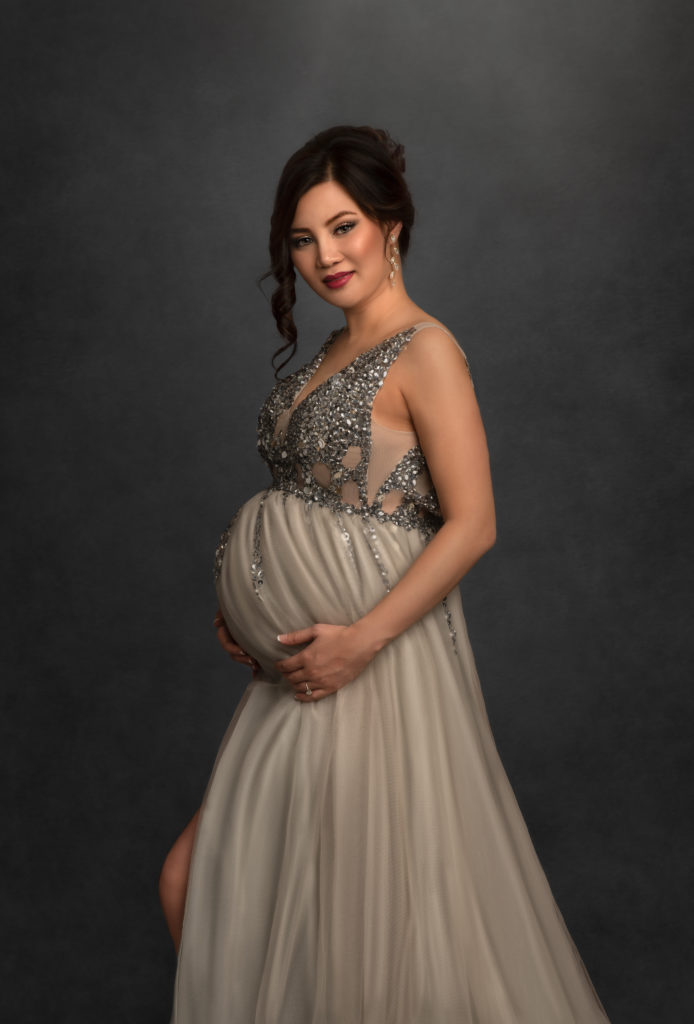 beautiful pregnant woman during fine art maternity photoshoot portrait session in studio with soft light and gorgeous maternity gown